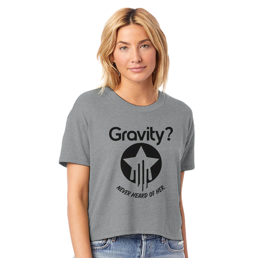 Model wearing a space gray cropped crewneck t-shirt with bold black text that reads “Gravity? Never Heard of Her.” and a star-and-streak icon, styled for flyers in the Hit Zero Co Flight Crew Certified capsule.