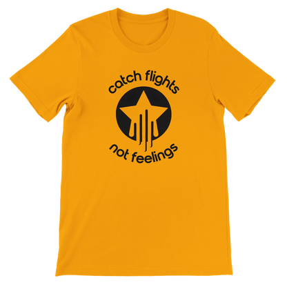 Gold unisex t-shirt with a bold black graphic that reads “catch flights not feelings” curved around a star and streak icon, printed on the chest.