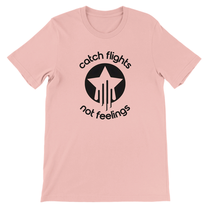 Soft pink unisex t-shirt with a bold black graphic that reads “catch flights not feelings” curved around a star and streak icon, printed on the chest.