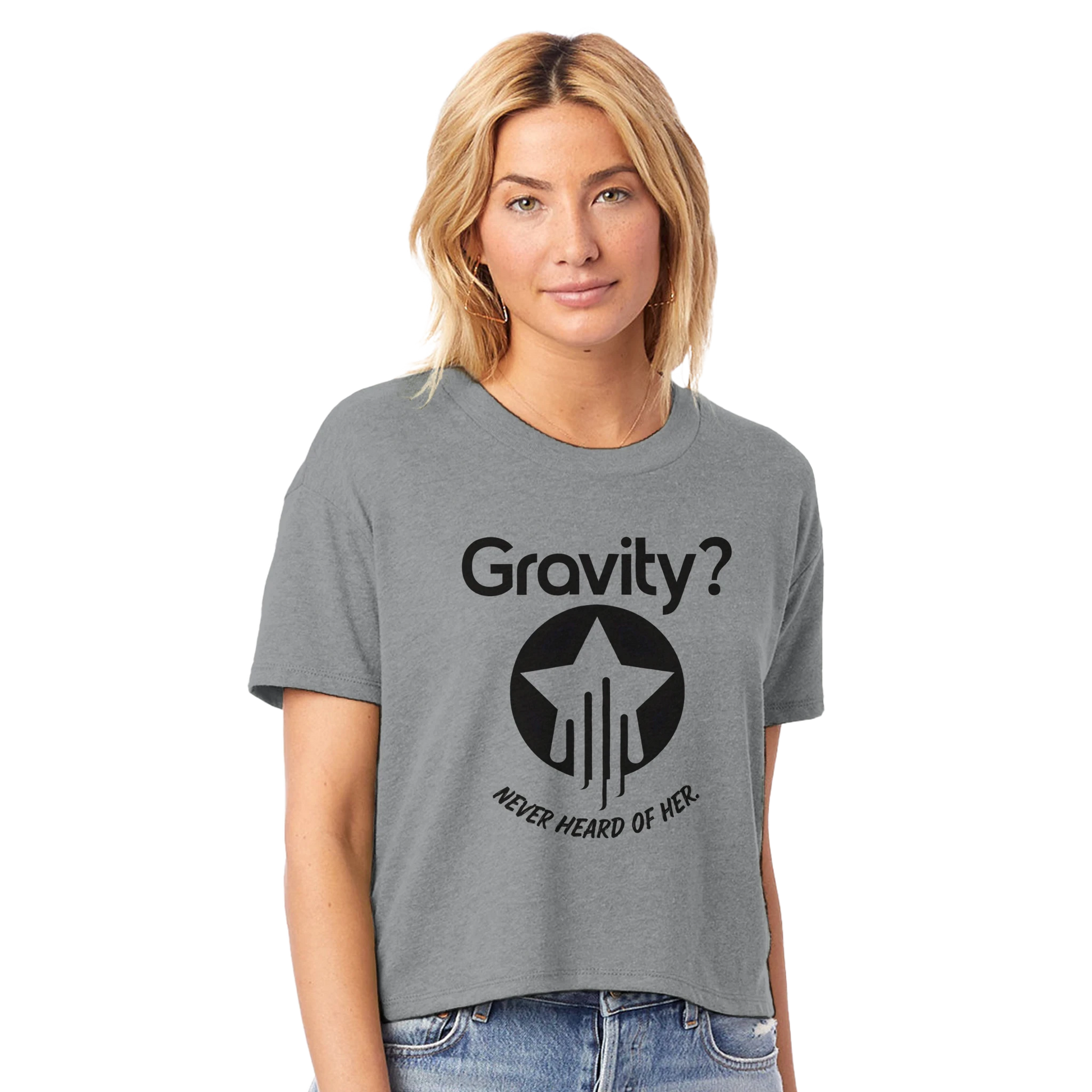 Model wearing a space gray cropped crewneck t-shirt with bold black text that reads “Gravity? Never Heard of Her.” and a star-and-streak icon, styled for flyers in the Hit Zero Co Flight Crew Certified capsule.
