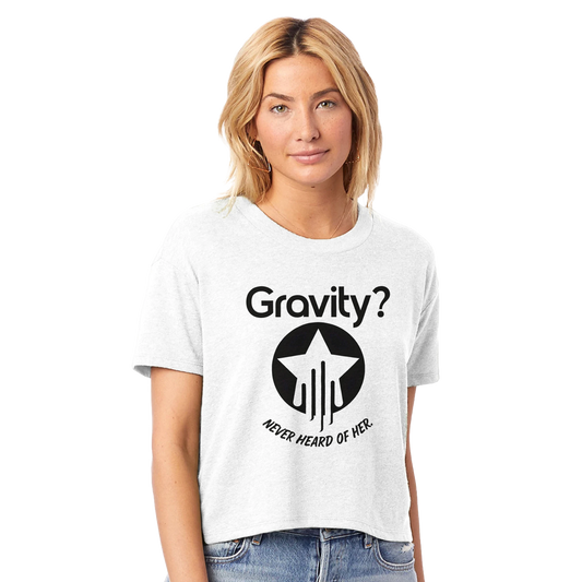 Model wearing a white cropped crewneck t-shirt with bold black text that reads “Gravity? Never Heard of Her.” and a star-and-streak icon, styled for flyers in the Hit Zero Co Flight Crew Certified capsule.